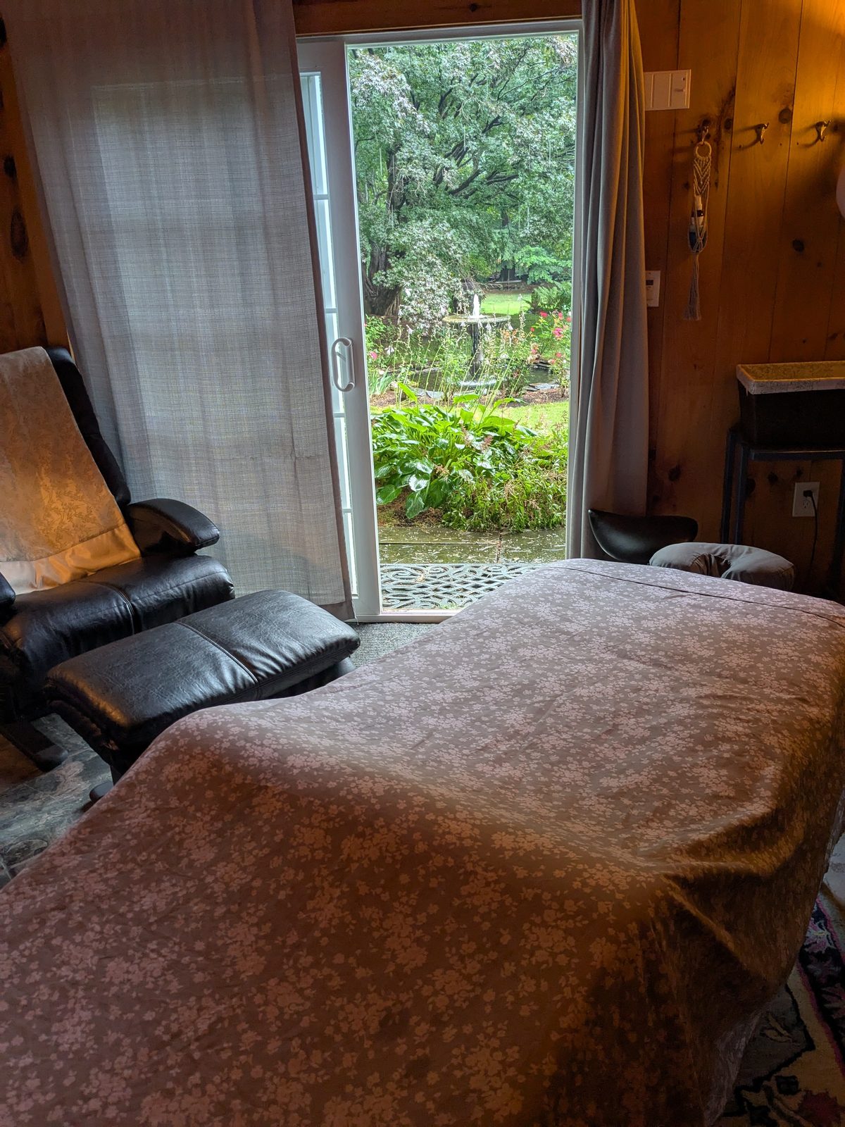 The treatment room with the glass door open onto a green garden, a
                  recliner beside it.